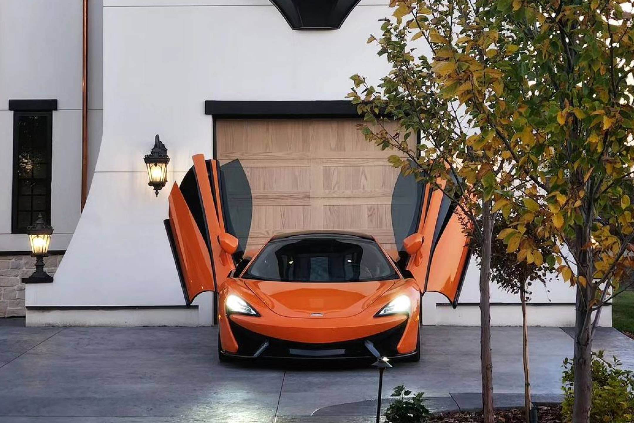 Orange car with open doors parked in front of a woodtones garage door