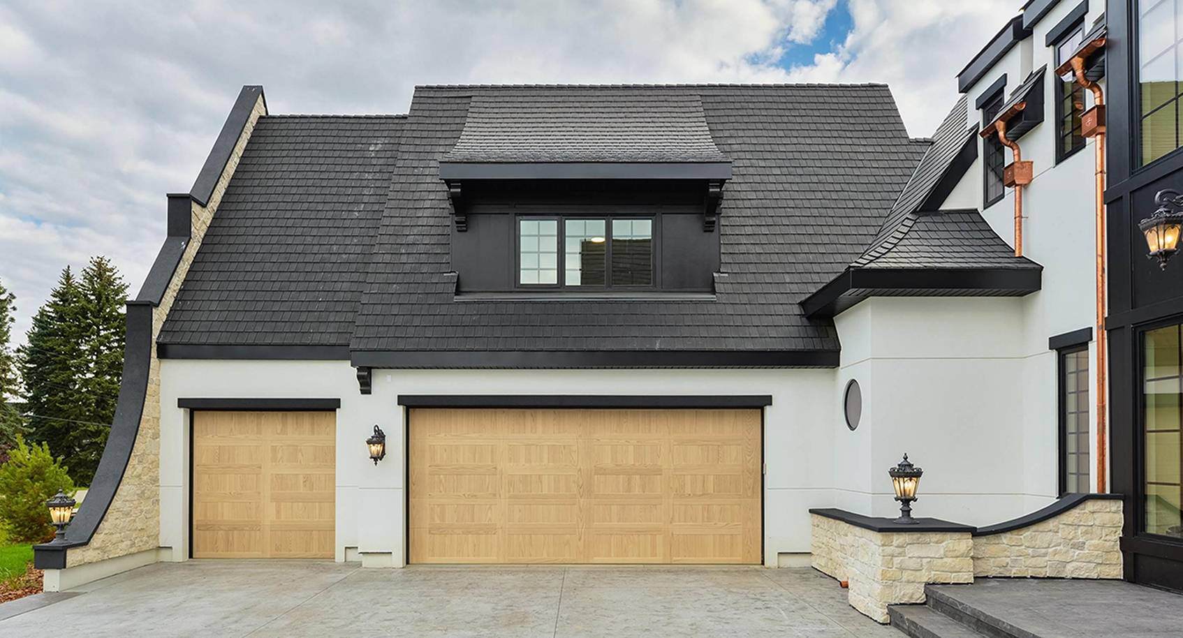 A black and white house with a sloped roof with two light woodtone garage doors
