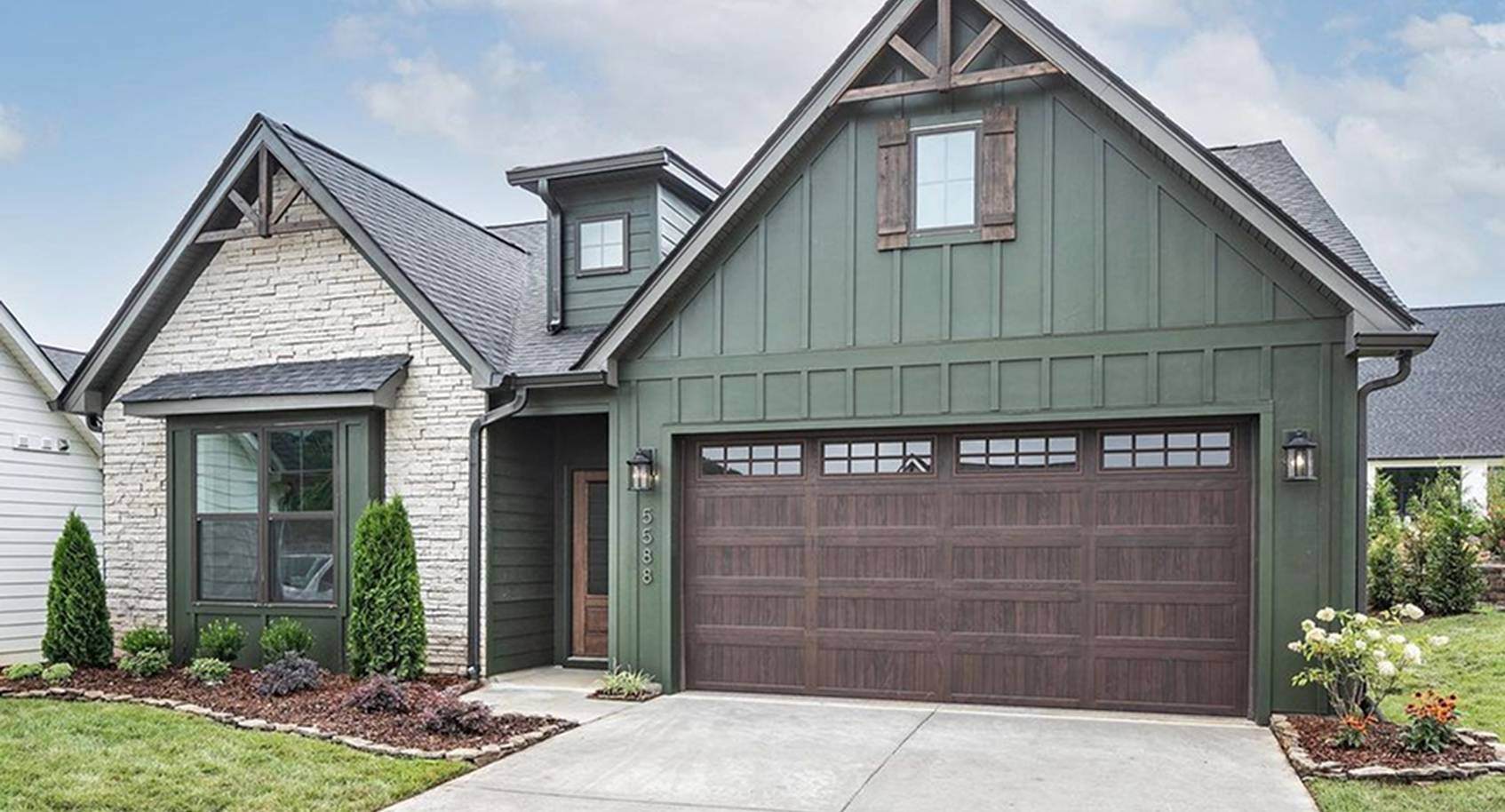 A green and brick modern tudor style house with a woodtone garage door