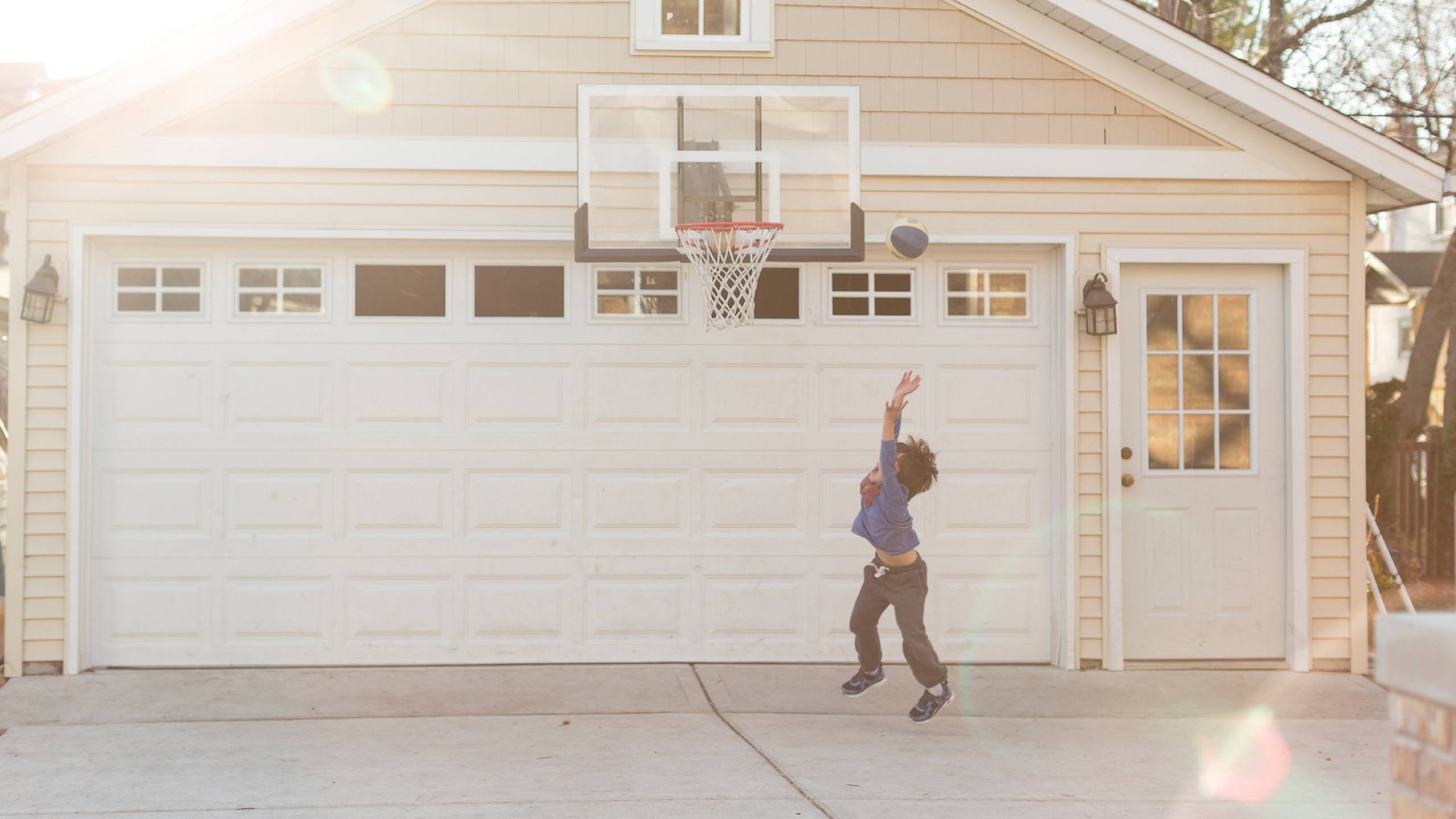 Boy playing basketball outside home in front of garage