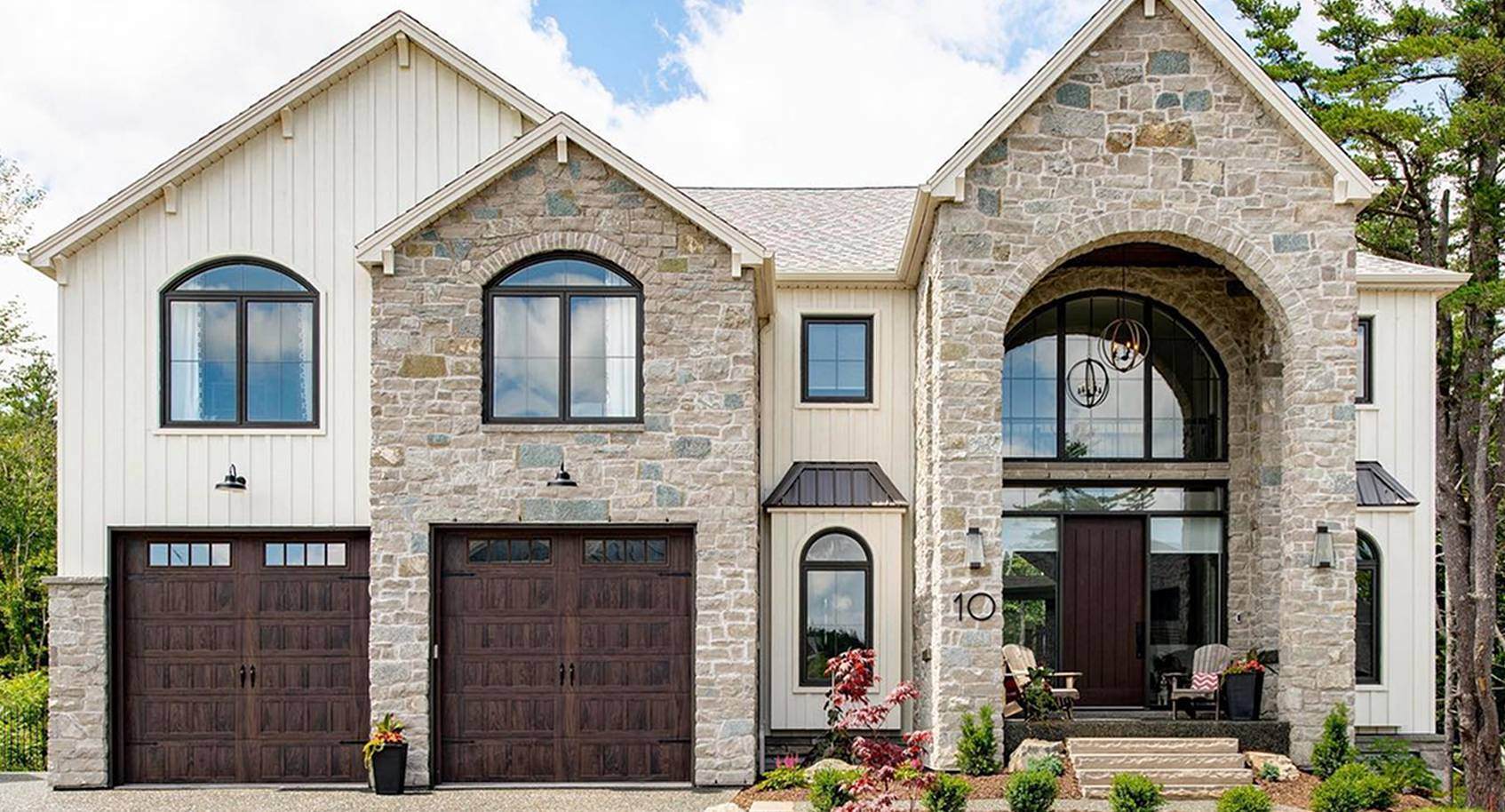 A light brick and white modern tudor house with two woodtone garage doors